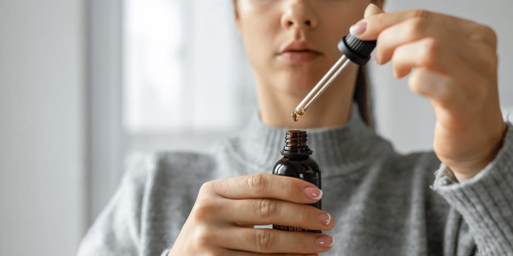 Vrouw met een druppelpipet boven een flesje olie van Hemp Clinic