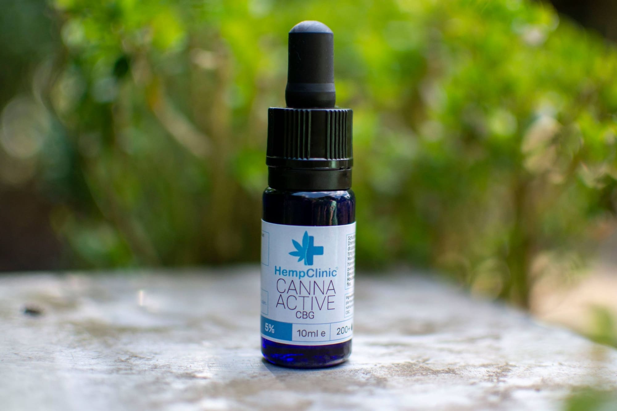 Flesje CannaActive CBG van Hemp Clinic op een stenen tafel voor groen blad