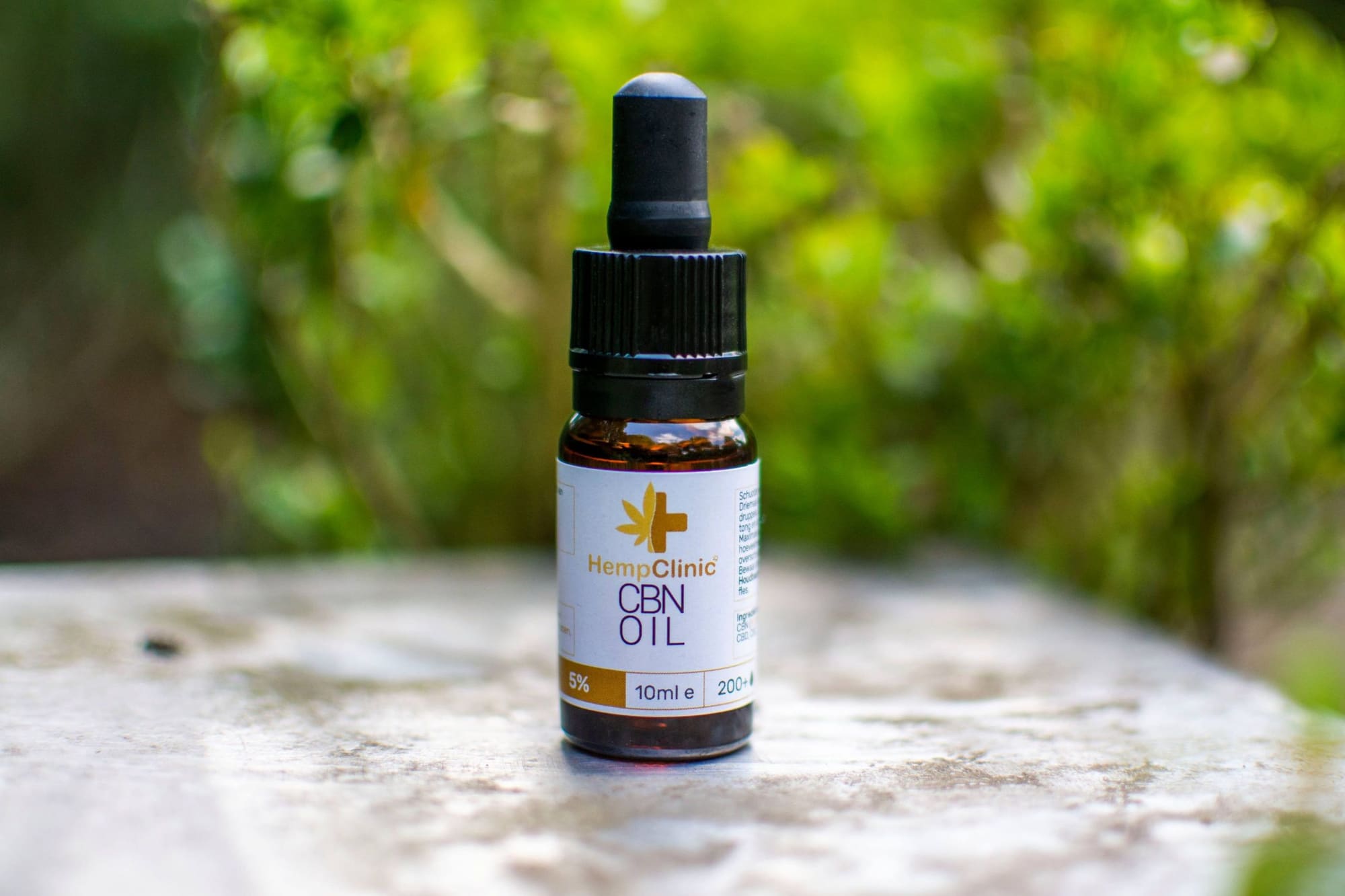 Flesje HempClinic CBN Oil op een stenen tafel tussen groene bladeren