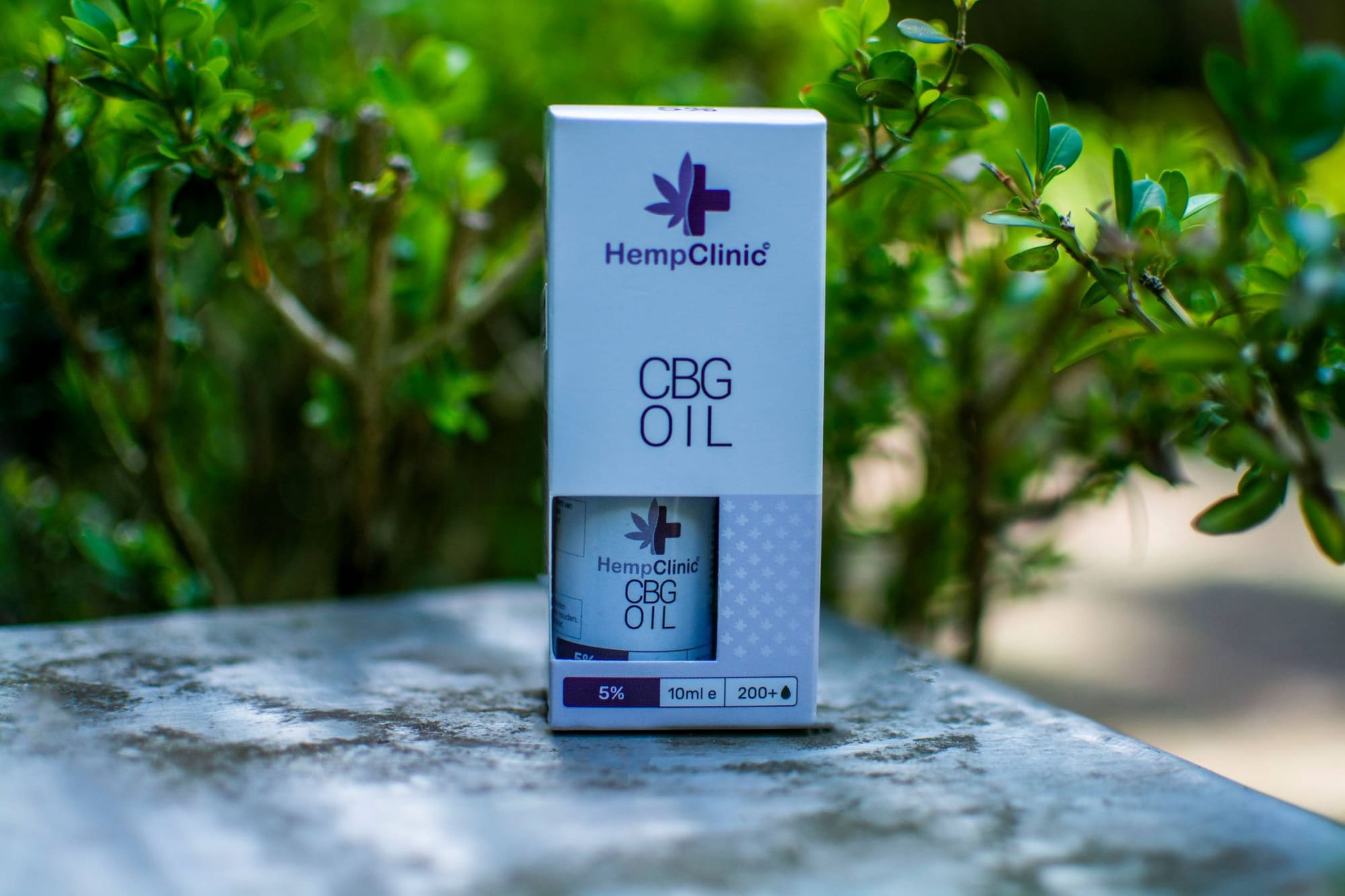 Doosje CBG olie van Hemp Clinic op een stenen tafel tussen de struiken